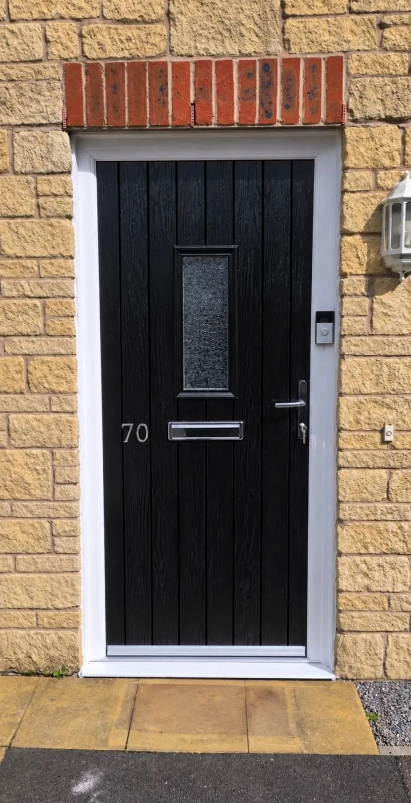 Black composite front door with obscure glass panel fitted to a stone-clad house